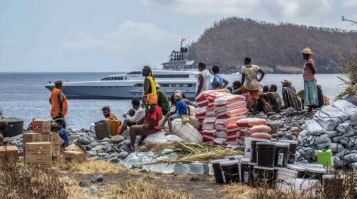 Locals receiving humanitarian aid with a luxurious yacht anchored in the background, symbolizing YachtAid Global's mission.